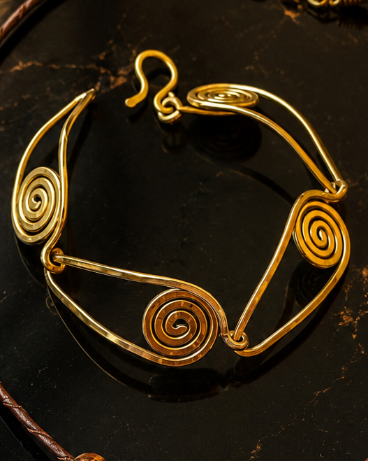 A jewelry set featuring a necklace, bracelet, and earrings with gold-toned spiral wire designs and dark brown wooden beads, displayed on a dark marble surface.