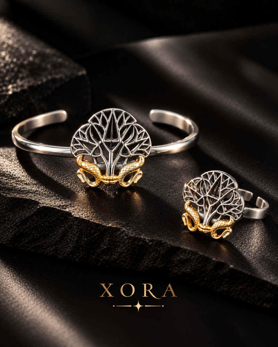 Silver and gold jewelry set by XORA, featuring a tree of life design with a snake wrapping around the trunk, displayed on a dark textured surface.