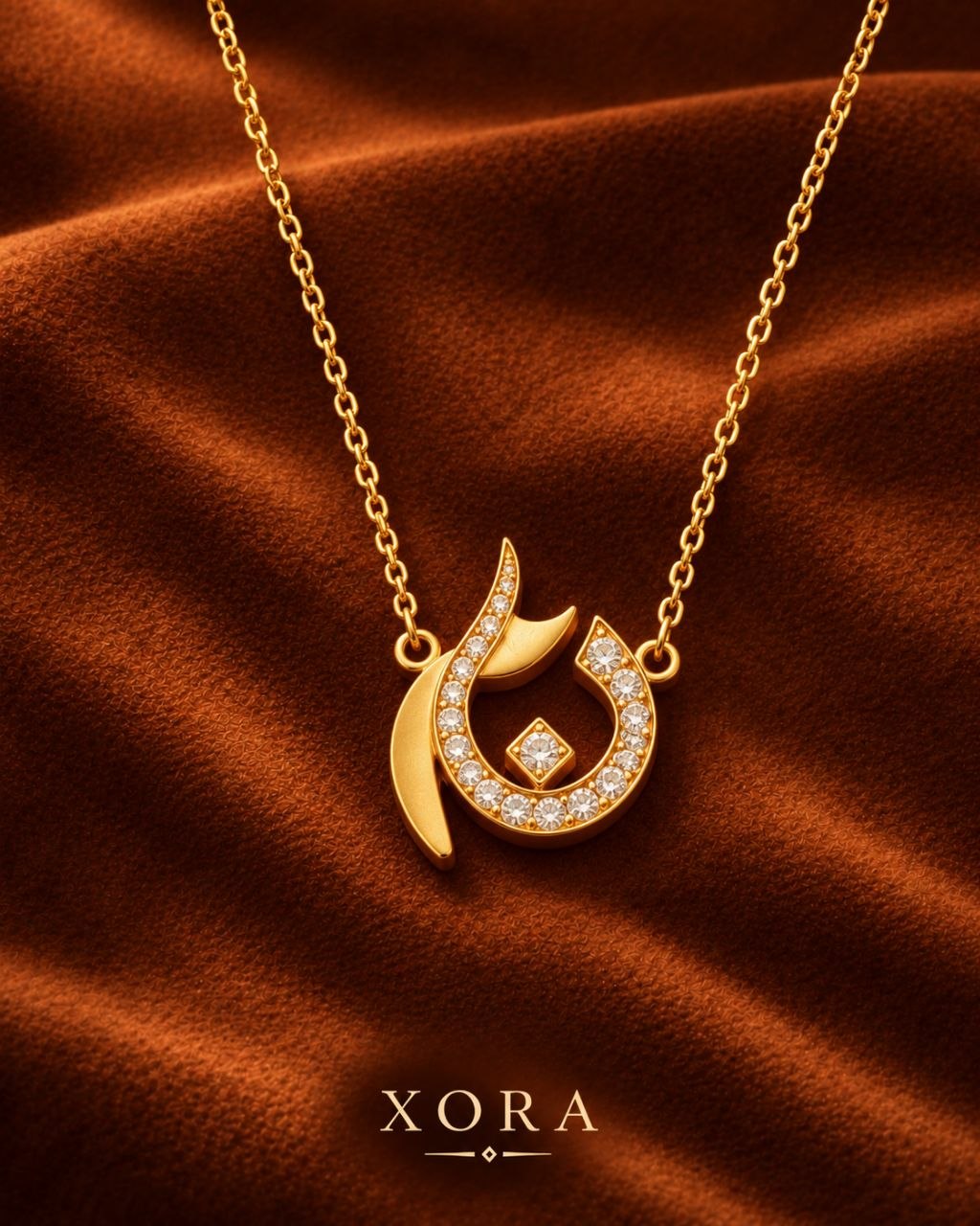 Gold pendant necklace with a crescent and leaf design set with small clear stones, displayed on a rich brown satin fabric background. The brand name XORA is printed at the bottom.