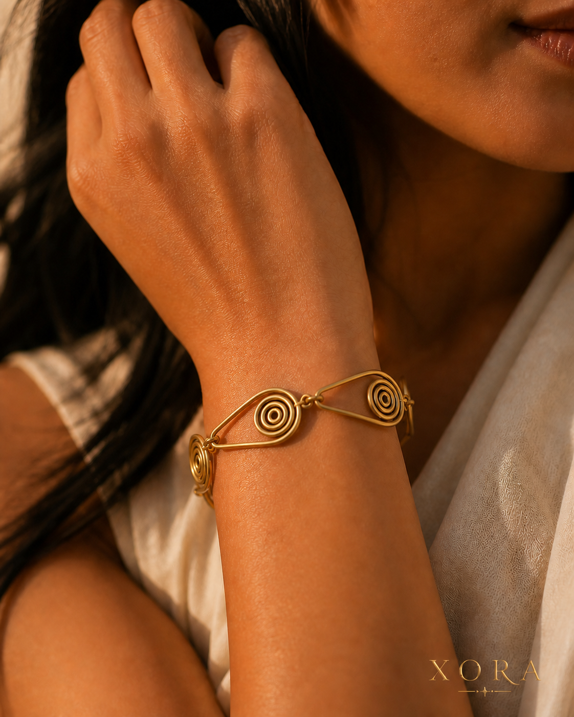 A close-up lifestyle shot of a woman wearing a gold wire bracelet with spiral details on her wrist, set against a warm, softly lit background with her hair and a white top visible.